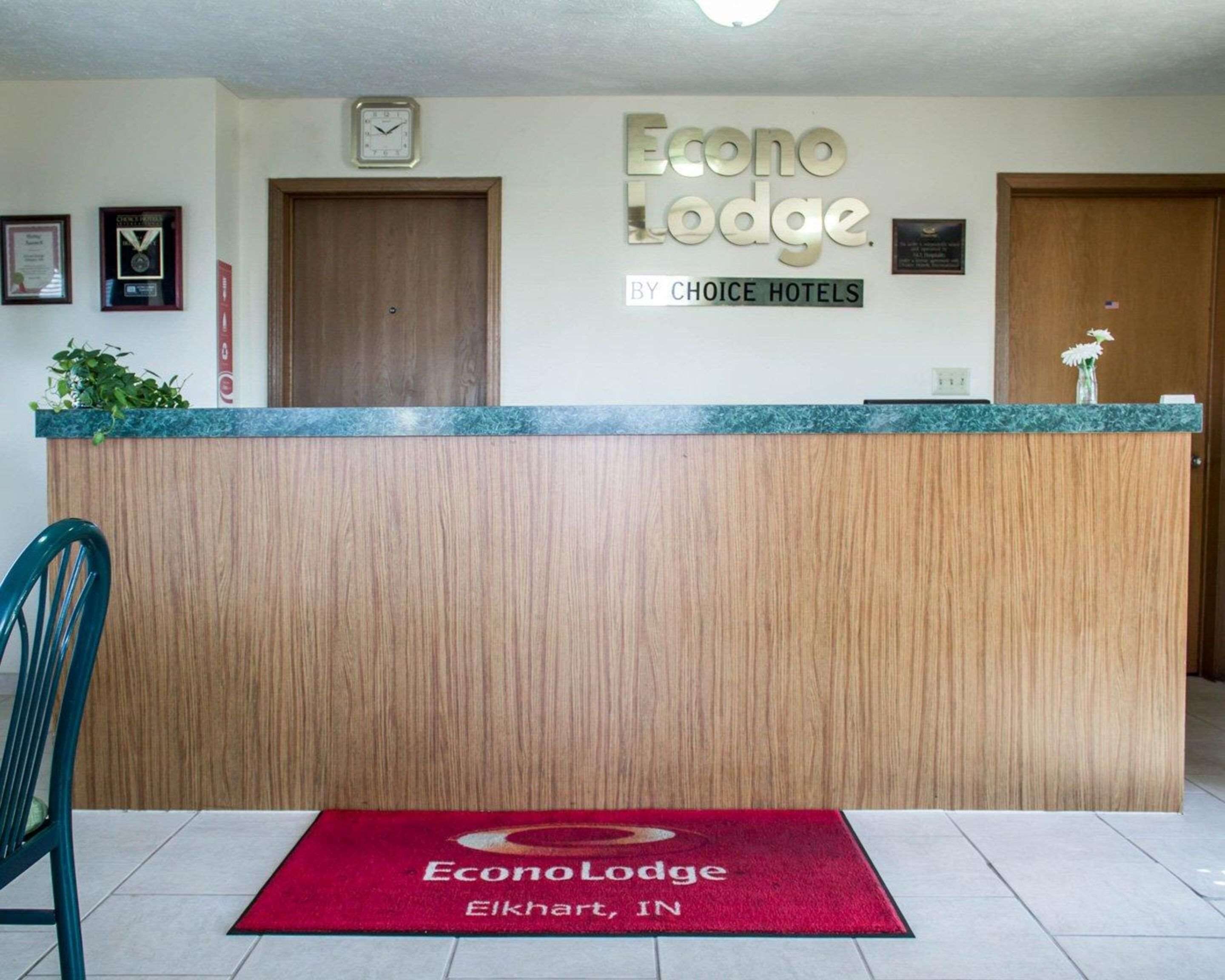 Una recepción en Econo Lodge, con un reloj encima, premios enmarcados en la pared y una alfombra roja con el nombre del hotel.