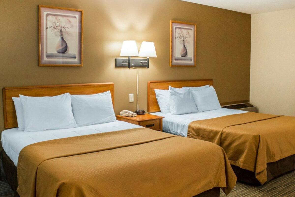 A hotel room with two beds, a nightstand with a lamp, and two framed pictures on the wall.