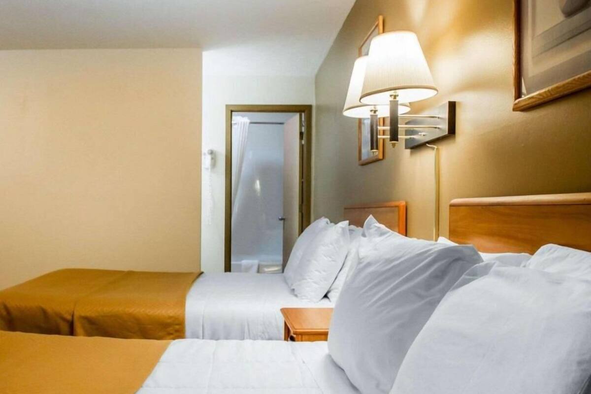 A hotel room with a bed, bedside table, lamp, and a door leading to a bathroom.