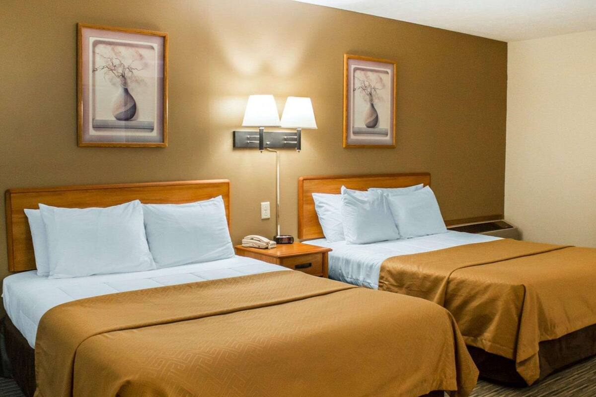 A hotel room with two beds, a nightstand with a phone, and two wall-mounted lamps.