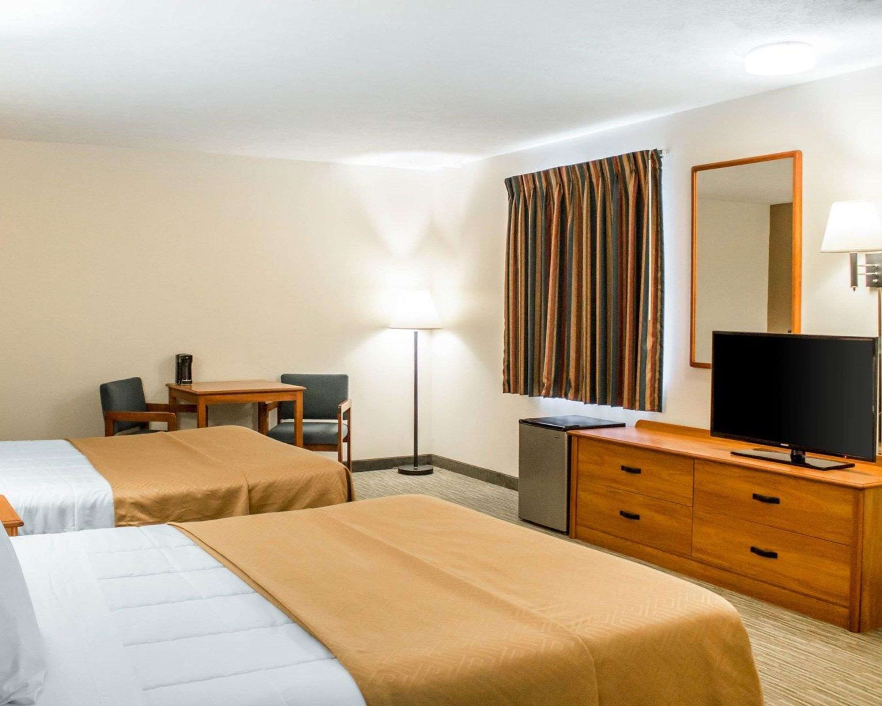Habitación de hotel con dos camas, un escritorio, una silla, un televisor, una lámpara y un espejo.