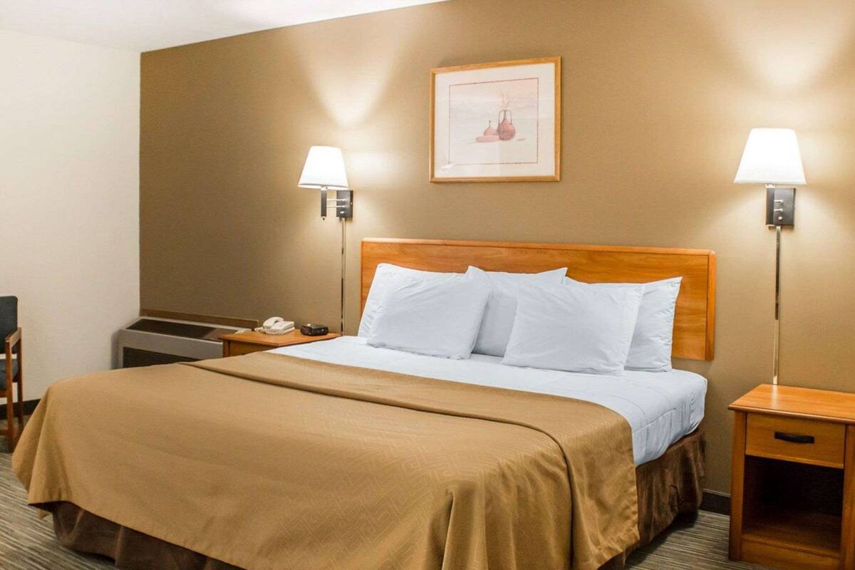 A hotel room with a large bed, two bedside lamps, a framed picture on the wall, and a small table with a phone and remote control.