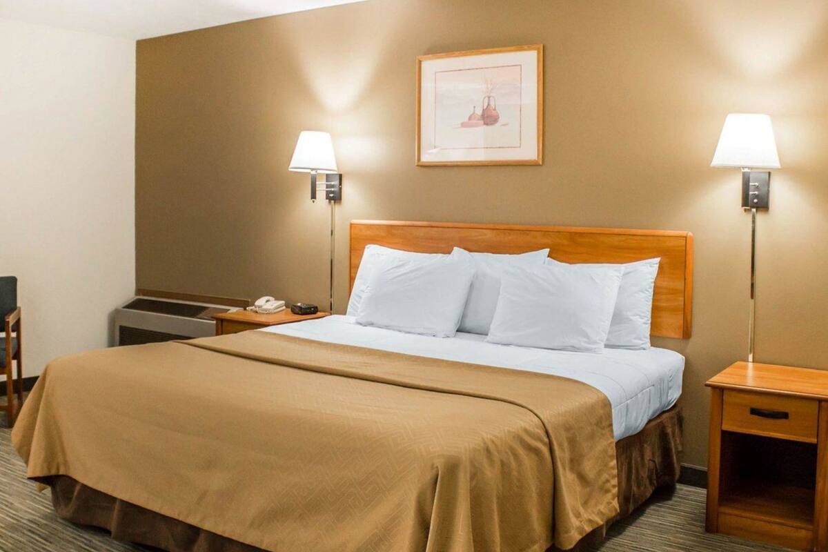 A hotel room with a large bed, two bedside lamps, a framed picture on the wall, and a small table with a phone and remote control.