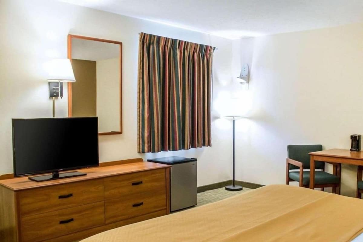 Een hotelkamer met een bed, een bureau, een televisie, een spiegel, een lamp en een raam met gordijnen.