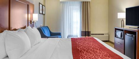 A hotel room with a large bed, a desk with a television, a chair, and a window with curtains.