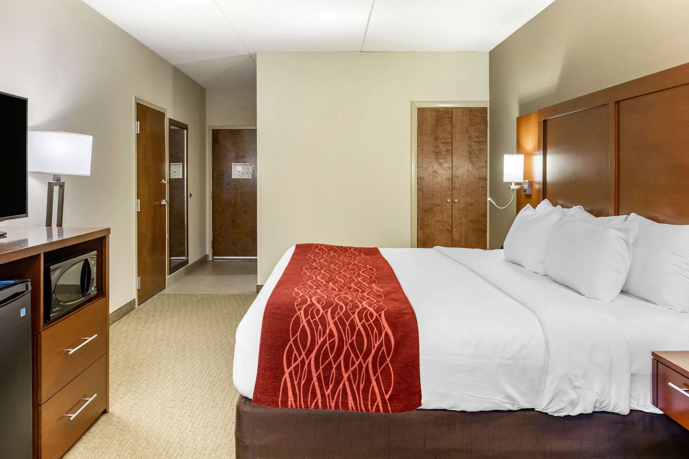 Una habitación de hotel con cama, televisión, escritorio con lámpara y microondas.