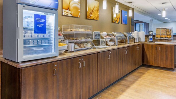 A breakfast buffet area with a refrigerated display case, various food stations, and wall-mounted light fixtures.