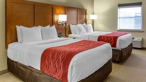 A hotel room with two beds, each with white linens and a red throw blanket. There are wall-mounted lamps and a window with a view.