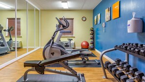 A gym with exercise equipment, a wall clock, and a hand sanitizer dispenser.