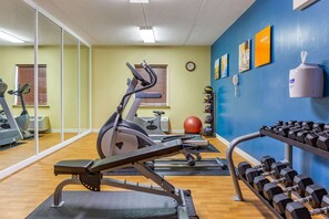 A gym with exercise equipment, a wall clock, and a hand sanitizer dispenser.