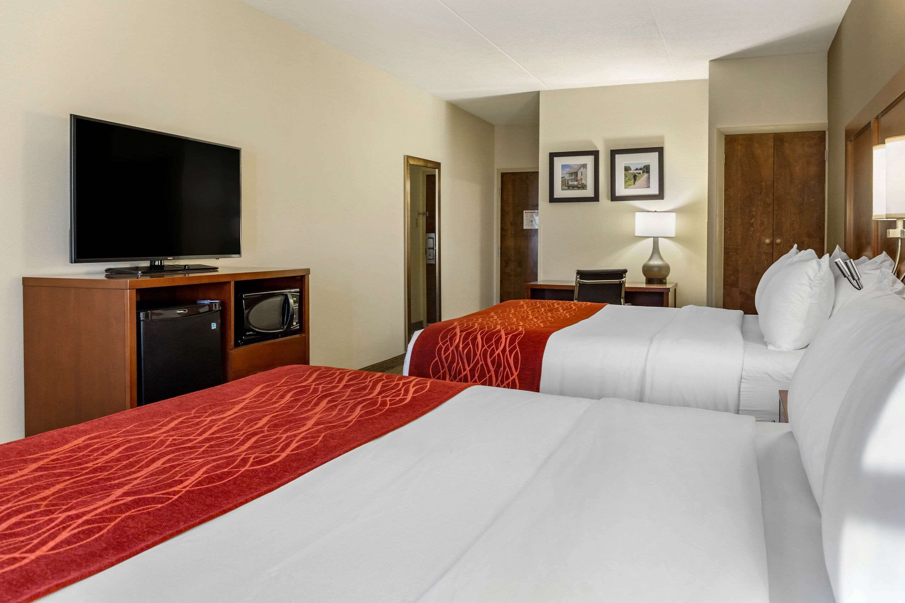 Quarto de hotel com duas camas, televisão, escrivaninha com luminária e porta para um banheiro.