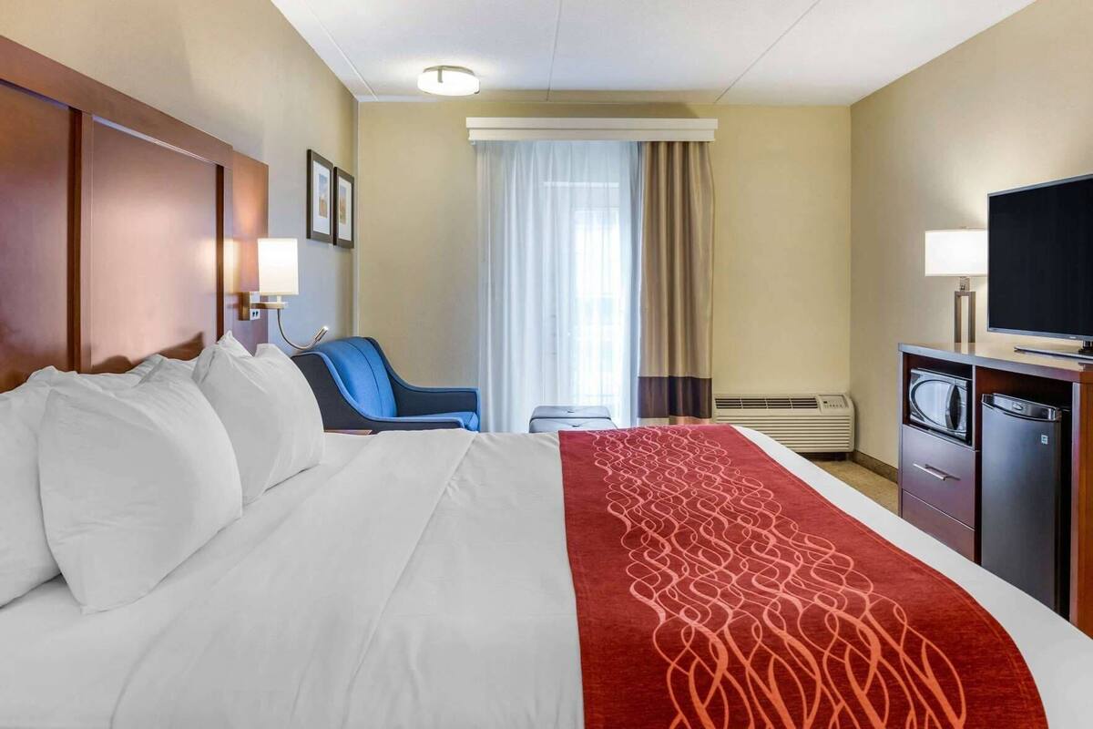 A hotel room with a bed, a desk with a TV, a chair, and a window with curtains.