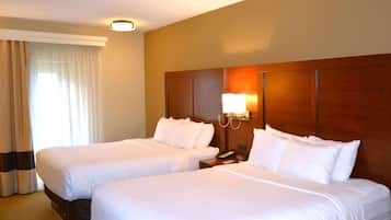 A hotel room with two beds, a nightstand with a phone, and a wall-mounted lamp.