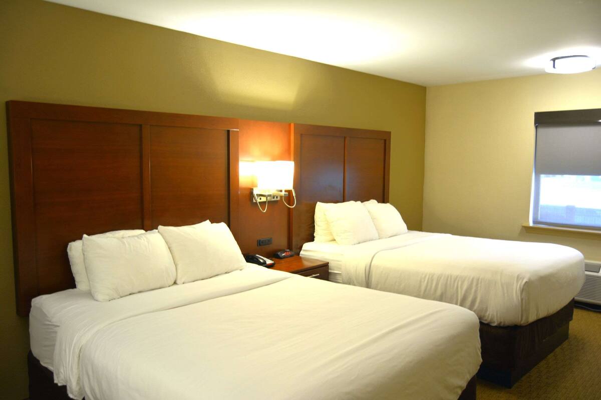 A hotel room with two beds, a nightstand, a lamp, and a window.