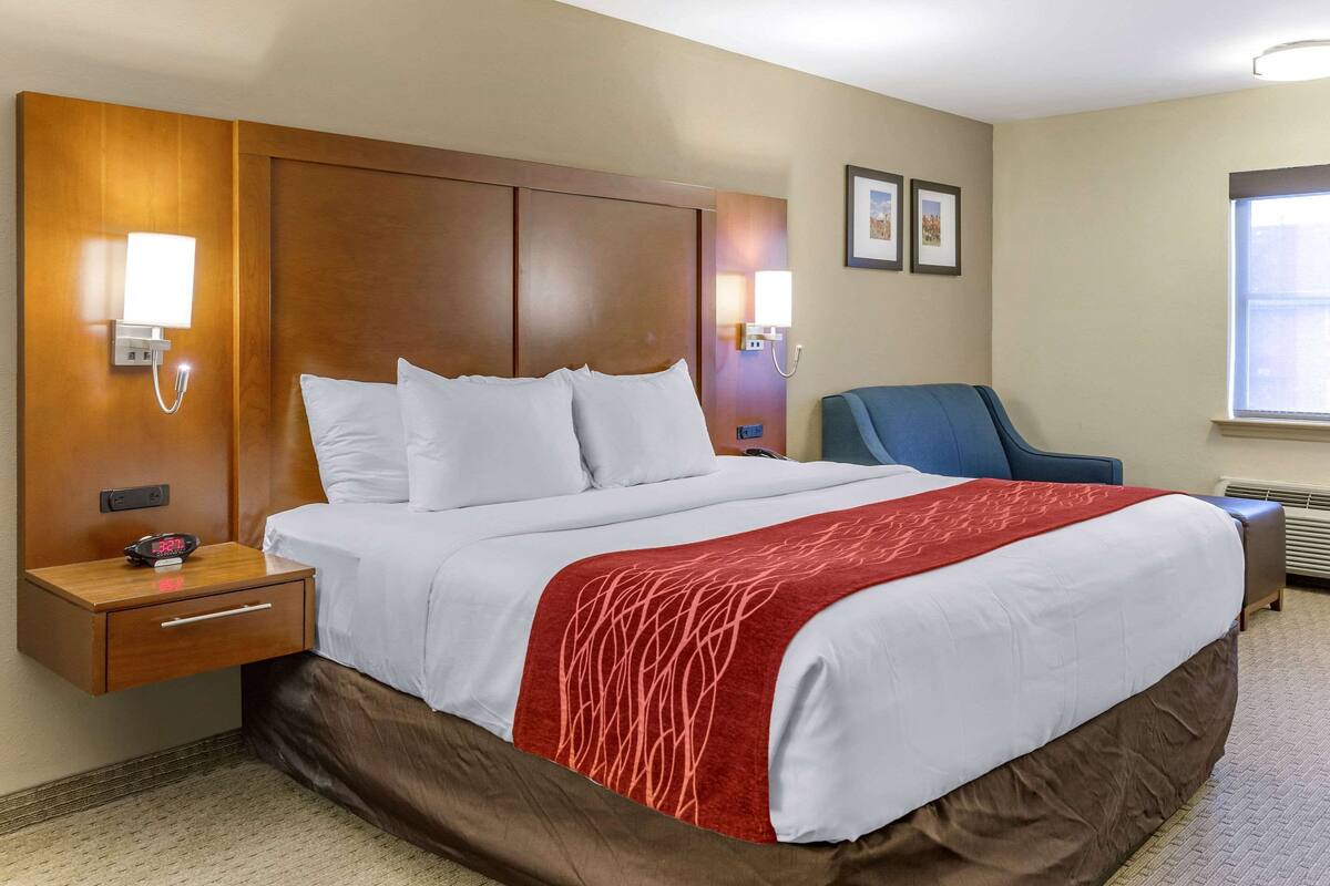 A hotel room with a large bed, a nightstand, a chair, and a window.