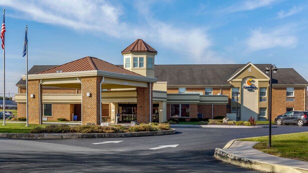 A hotel with a covered entrance, a small tower, and a parking lot.