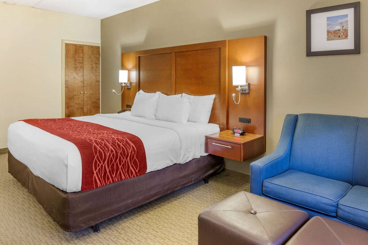 A hotel room with a large bed, a wooden headboard, bedside lamps, a blue armchair, and a small table.
