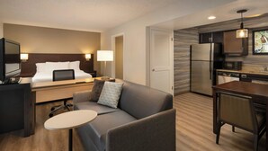 A modern hotel room with a bed, a sofa, a small table, a TV, a desk, a lamp, a kitchen area with a refrigerator, microwave, and sink. - Residence Inn by Marriott Anaheim Placentia Fullerton (Placentia)
