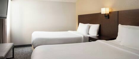 A hotel room with two beds, a nightstand, a lamp, and a window with curtains.