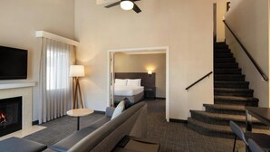 A modern hotel room with a living area featuring a sofa, a flat-screen TV, a fireplace, and a ceiling fan. - Residence Inn by Marriott Anaheim Placentia Fullerton (Placentia)