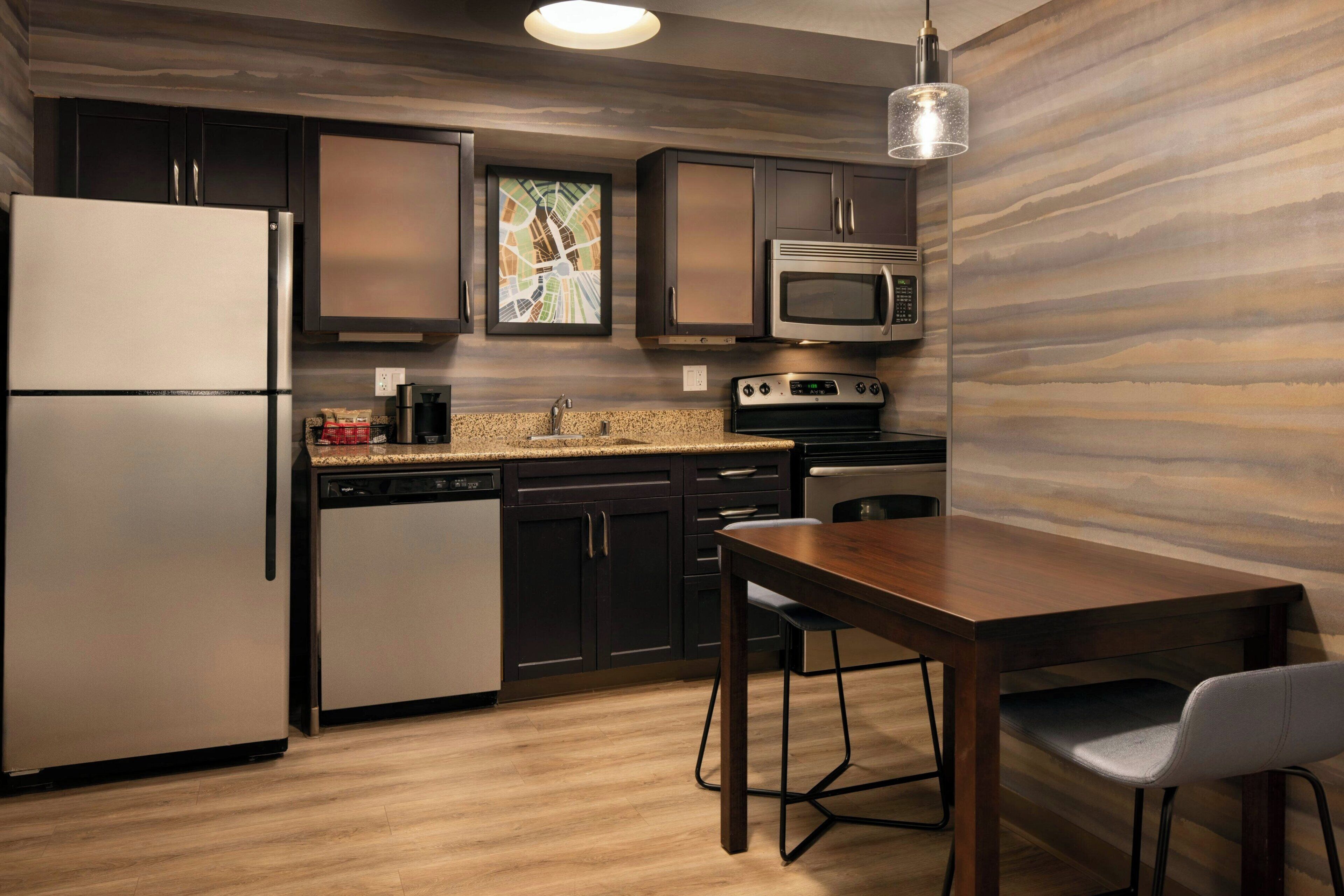 A modern kitchen with stainless steel appliances, dark cabinetry, and a wooden dining table.