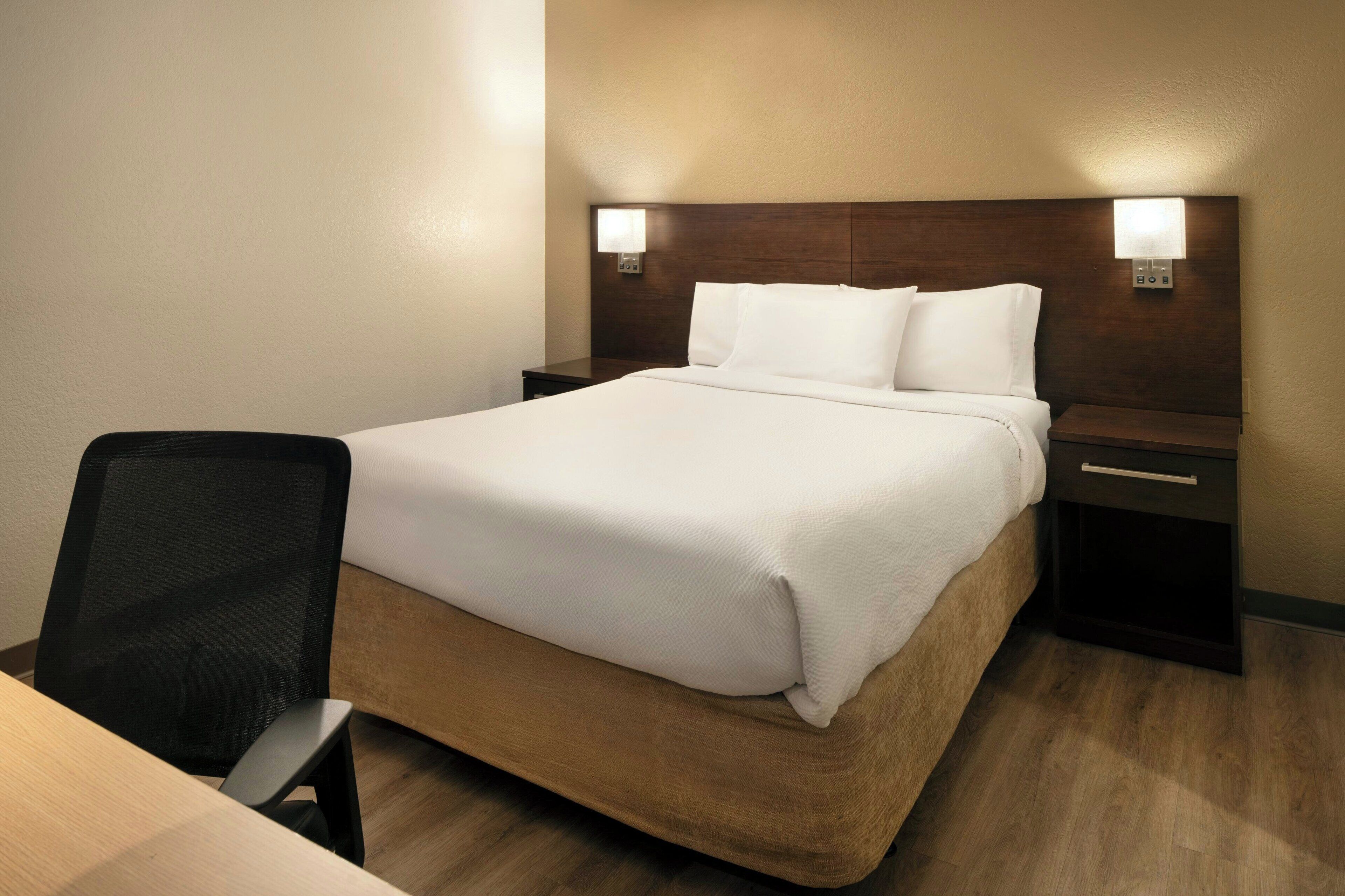 Ein Hotelzimmer mit einem großen Bett, einem Schreibtisch und einem Stuhl. Zwei Nachttische mit Lampen sind vorhanden.