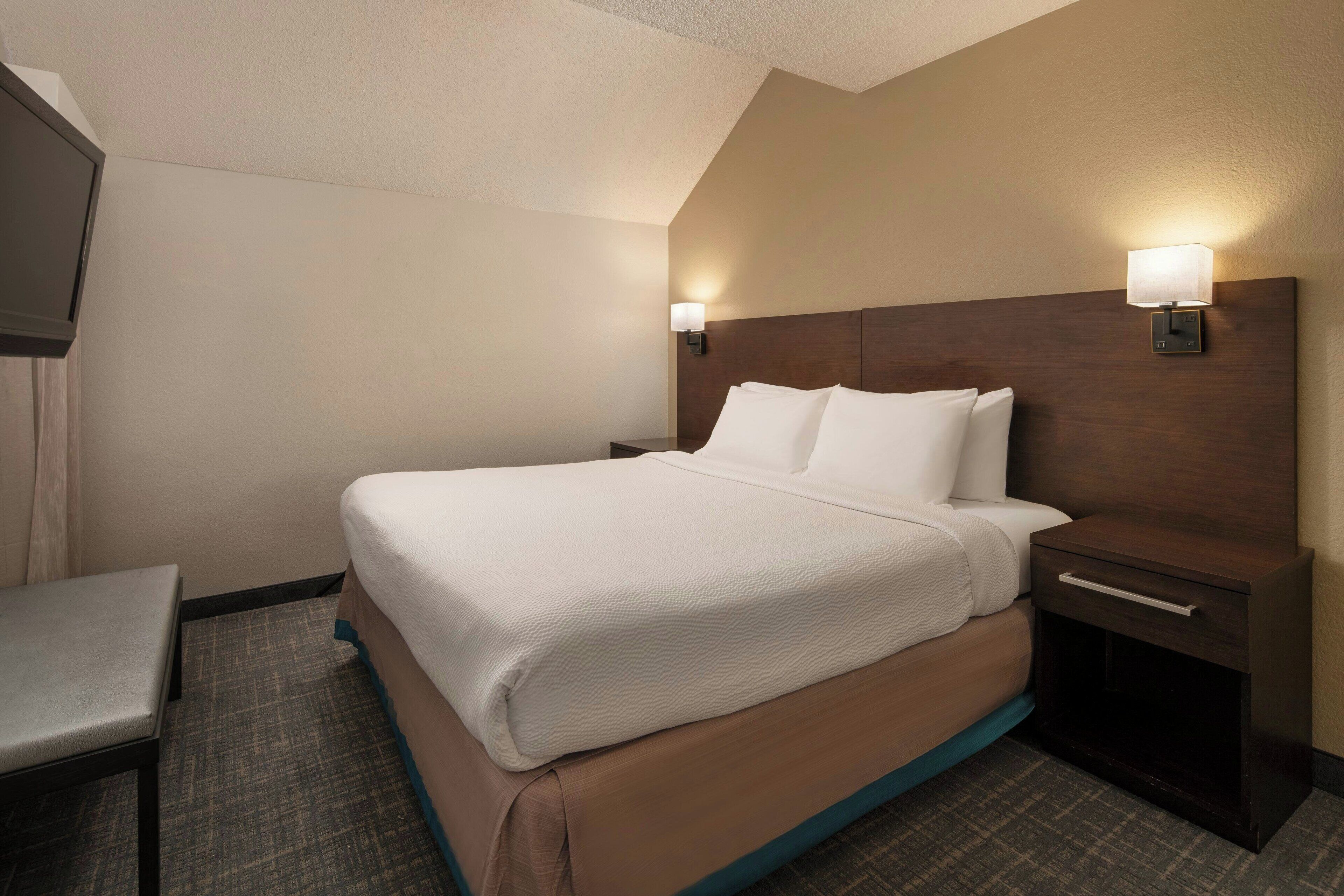Une chambre d’hôtel avec un grand lit, une table de chevet, une chaise et une lampe fixée au mur.