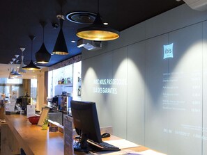 Zona de recepción de hotel con diseño moderno, que incluye luces colgantes y un panel de información digital.