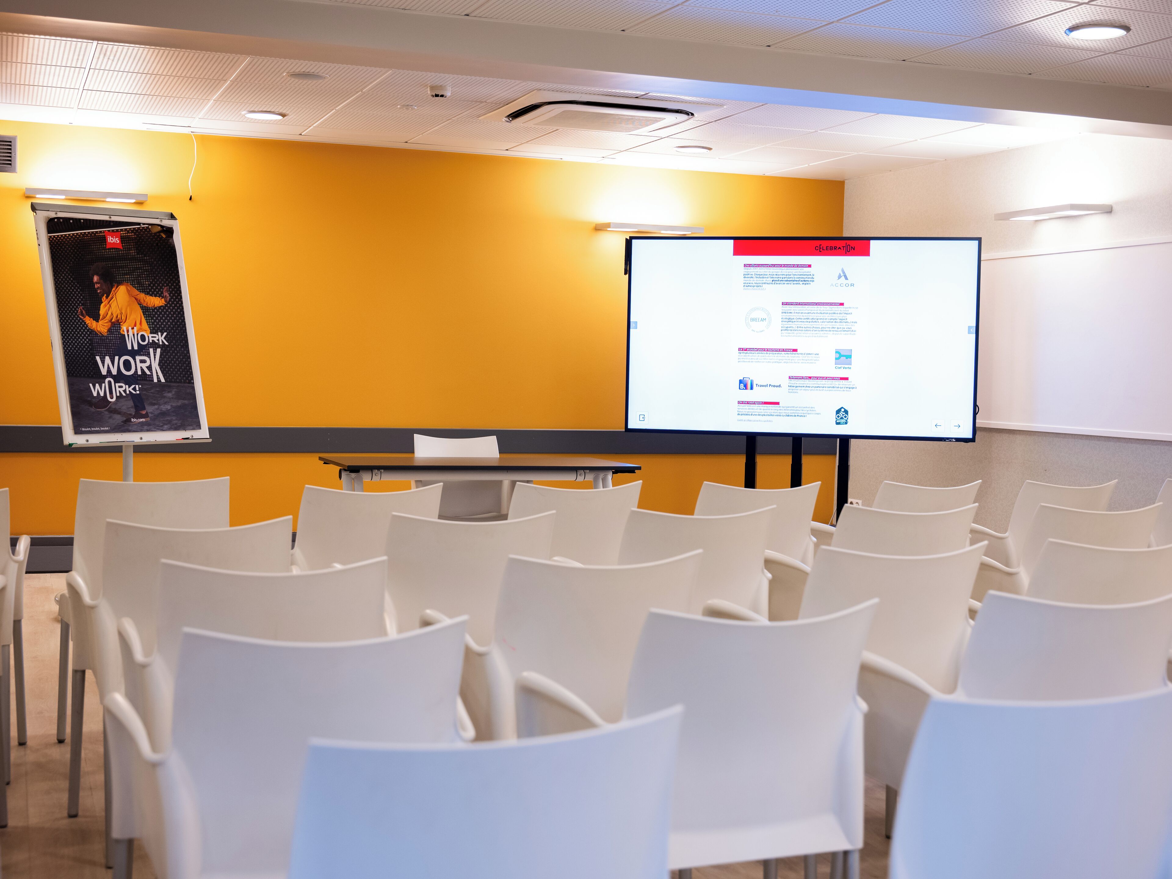Un salón de conferencias con sillas blancas, una pantalla de proyector y una presentación en la pared.