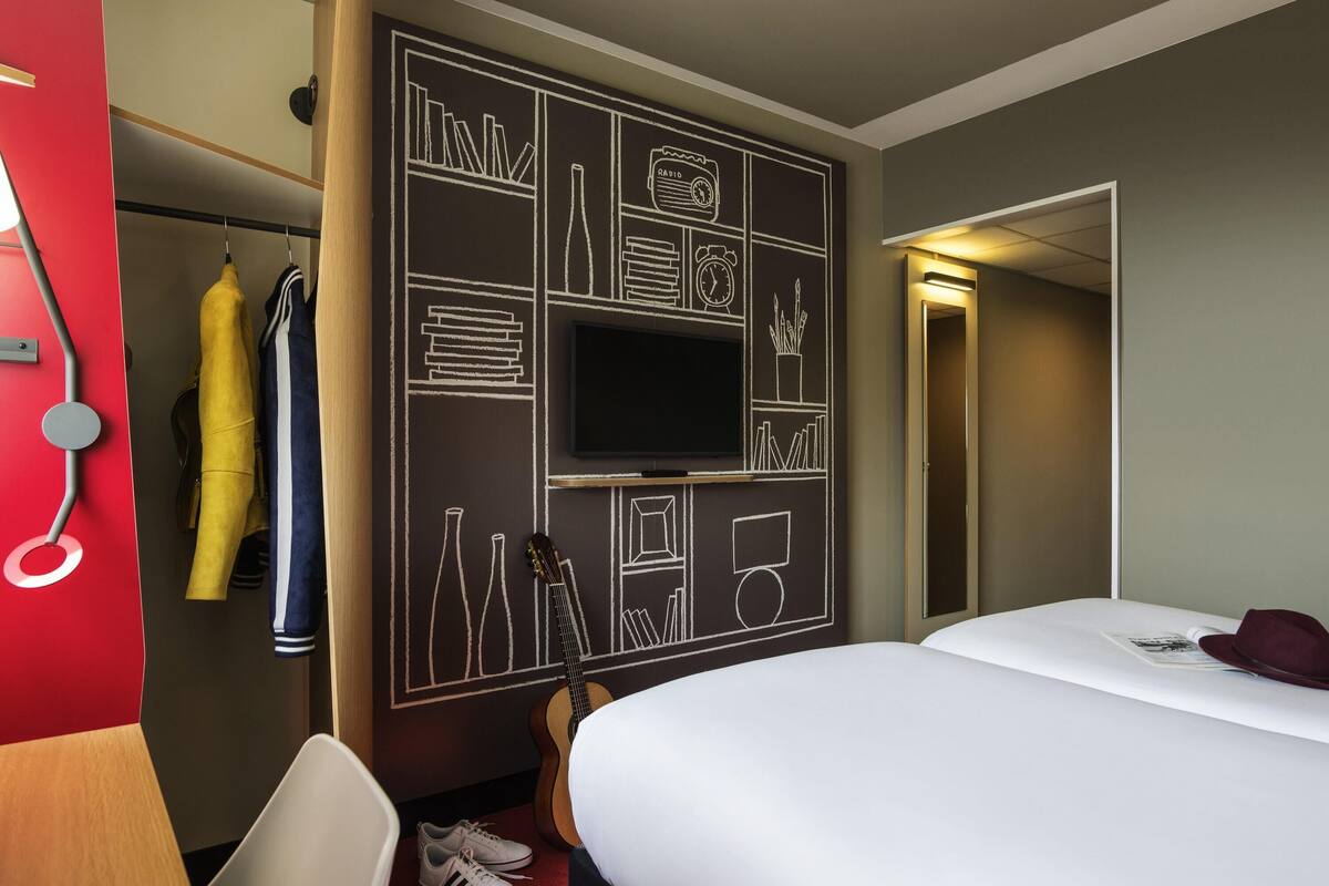 A hotel room with a bed, a TV, a wardrobe, and a red wall with a chalkboard design.