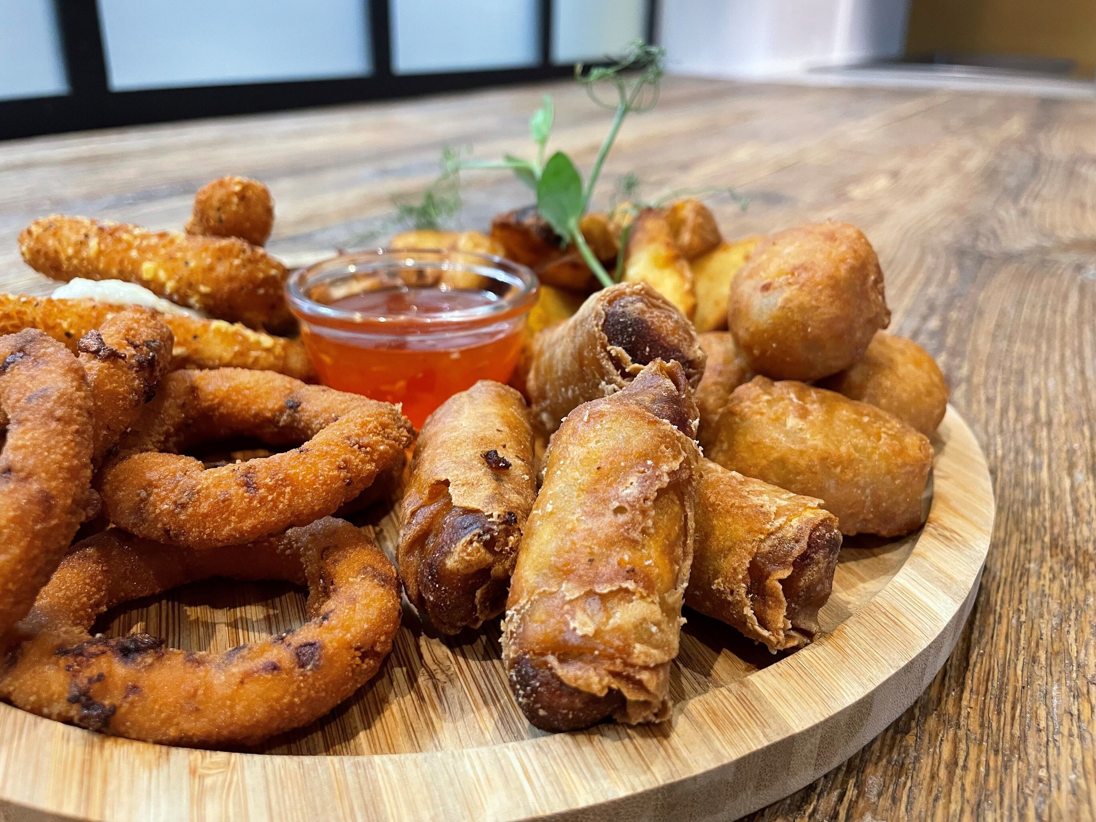 Una tabla de madera con diversos aperitivos fritos y un recipiente pequeño para salsa.