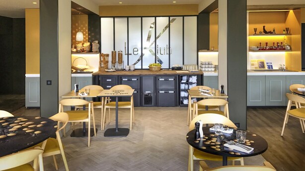 Un bar moderno con barra, taburetes y una pared decorativa con la palabra 'Le Club'.
