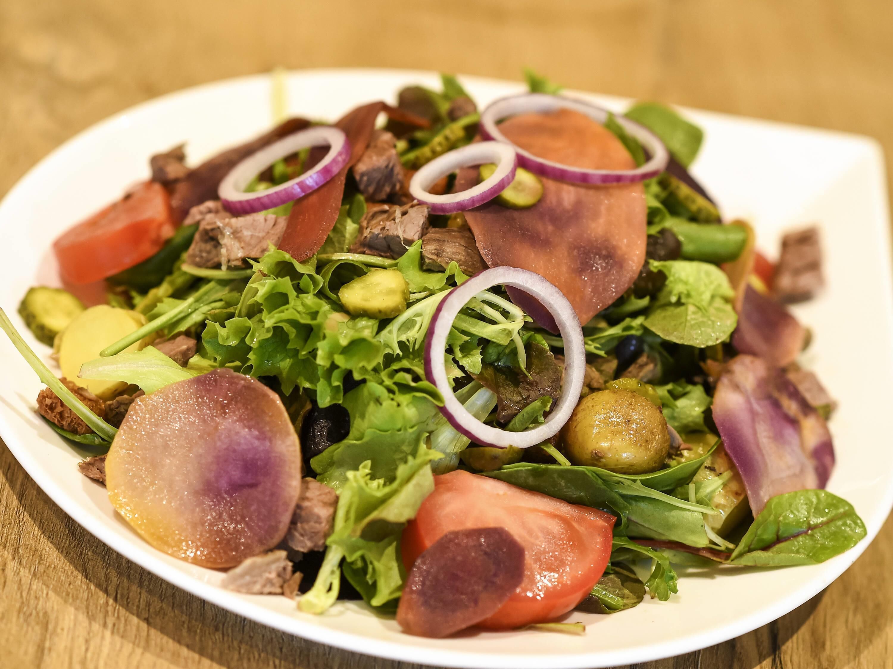 Uma salada de folhas verdes variadas com tomates, cebolas e azeitonas.