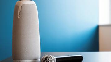A white smart speaker and a black microphone on a table against a blue wall.