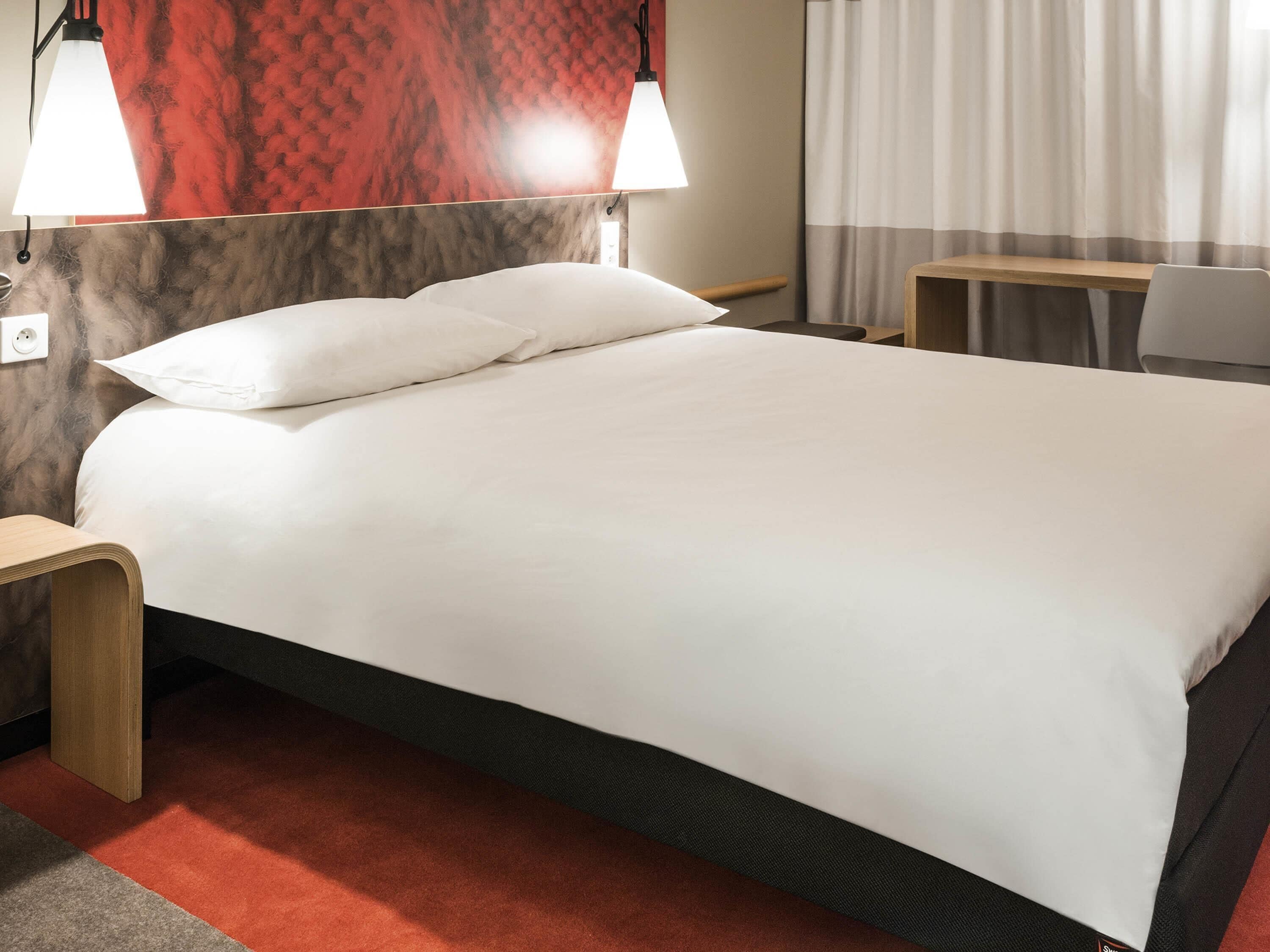 Una habitación de hotel con una cama, dos lámparas de noche, un escritorio y una silla.