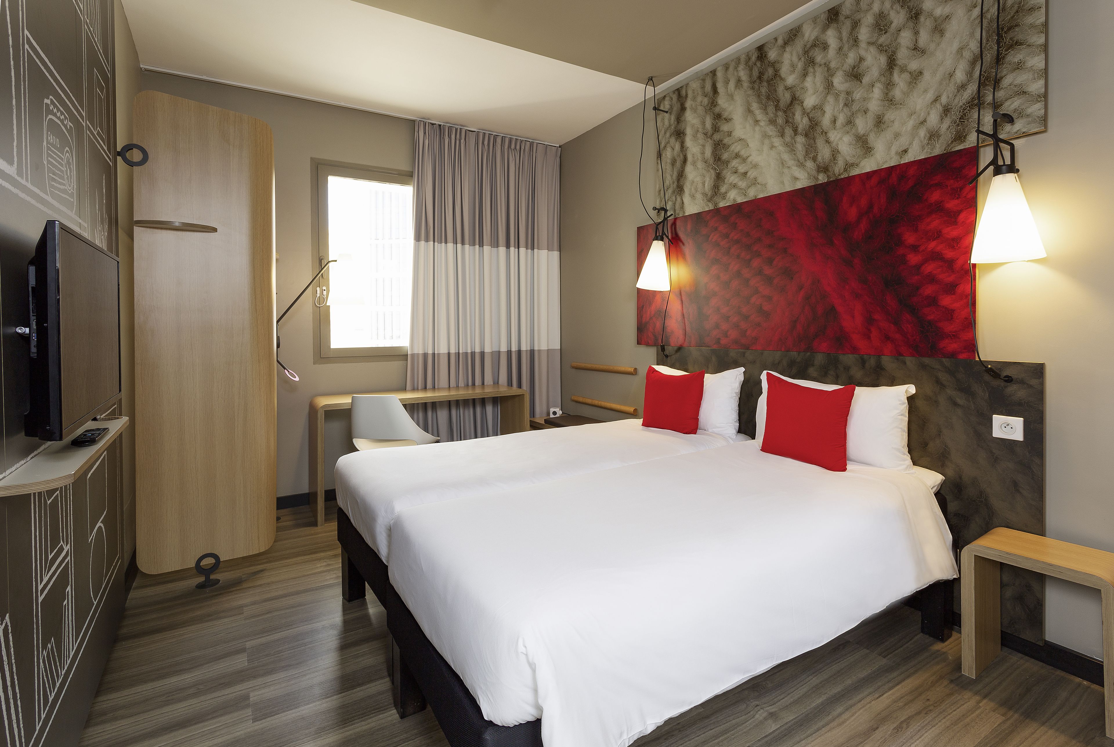A modern hotel room with a large bed, a desk, a TV, and a window with curtains.