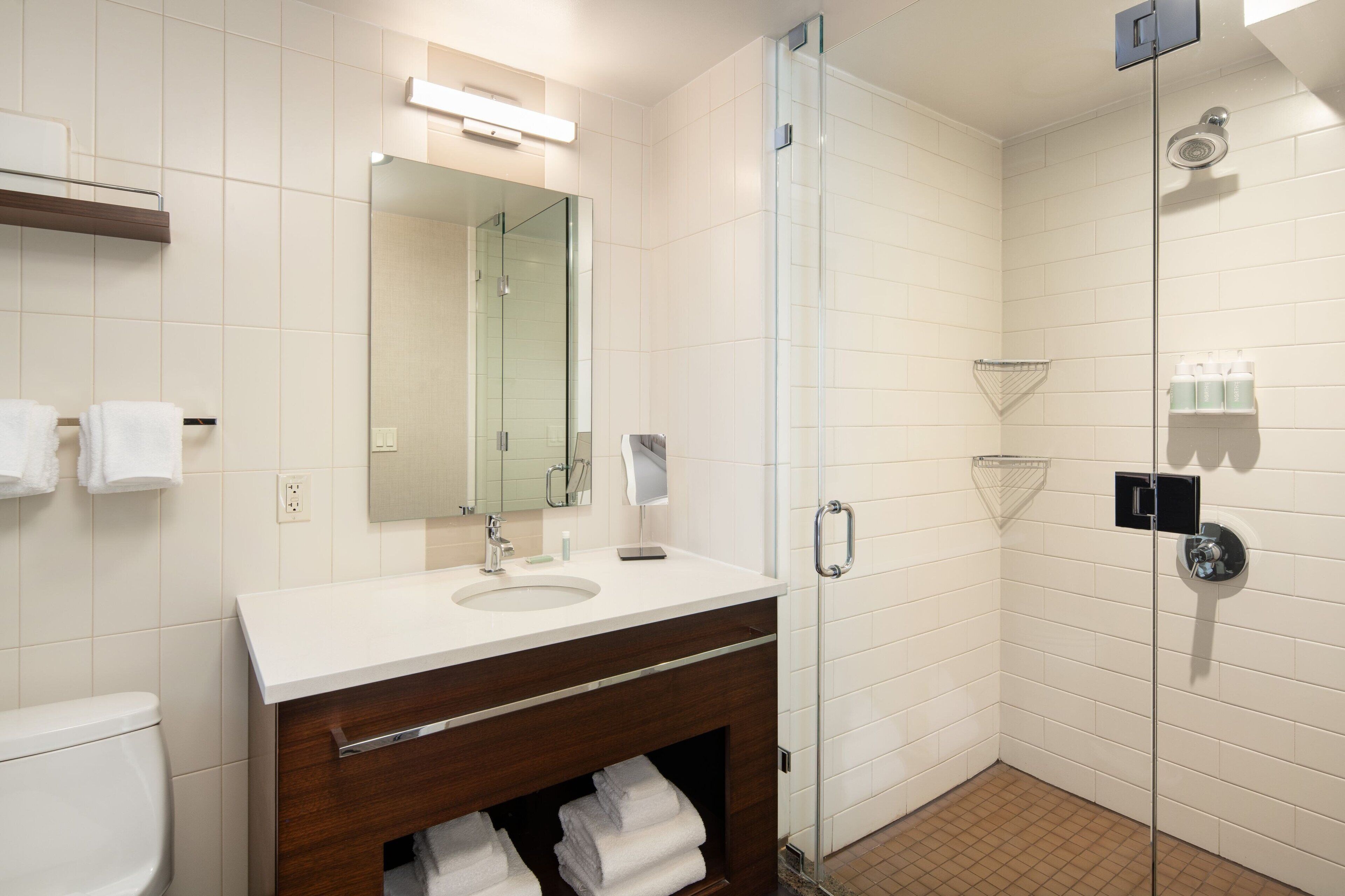 A modern bathroom with a glass-enclosed shower, a large mirror, and a vanity with a sink and towel rack.