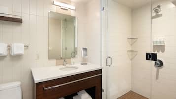 A modern bathroom with a glass-enclosed shower, a large mirror, and a vanity with a sink and towel rack.