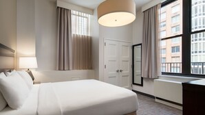 Una habitación de hotel con una cama grande, un escritorio, una lámpara, un armario y una ventana con cortinas.