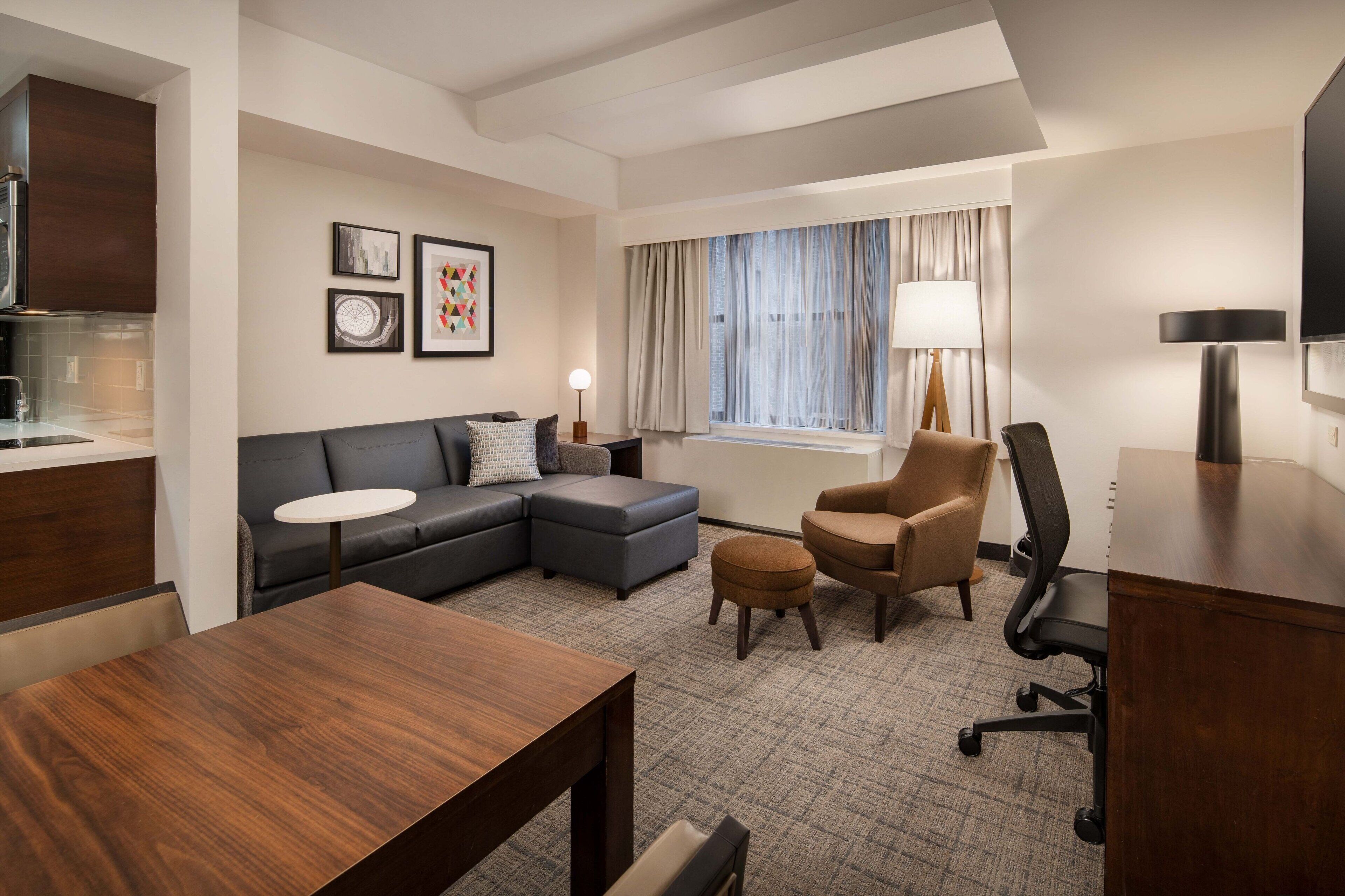 Een moderne hotelkamer met een bank, poef, fauteuil, bureau en een flatscreen televisie.
