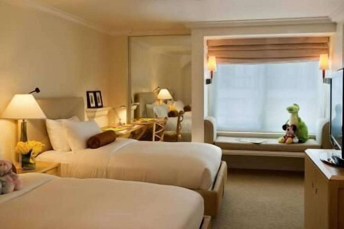A hotel room with two beds, a desk, a chair, a window with a view, and a television.
