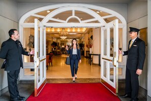 A grand entrance with a red carpet leading to a well-lit interior. Two uniformed staff members are present, one holding a door open and the other standing by. - Taj Campton Place (San Francisco)