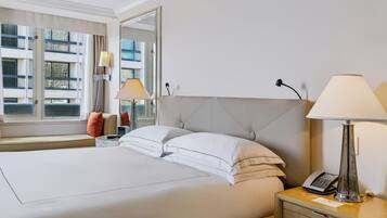 A hotel room with a large bed, bedside lamps, a nightstand with a phone, and a window with a view of buildings.