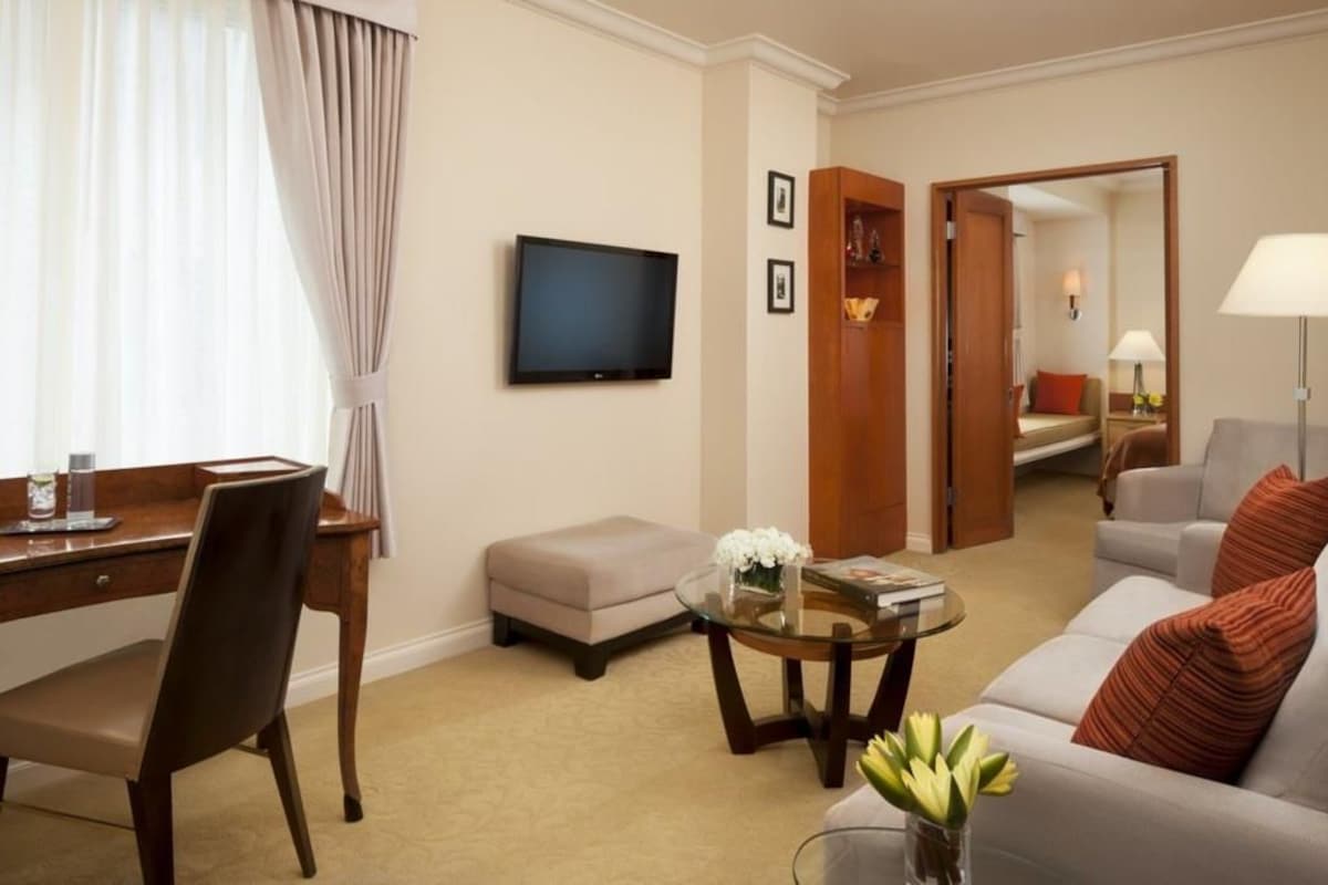 A hotel room with a desk, chair, television, sofa, and a small table with a vase of flowers.