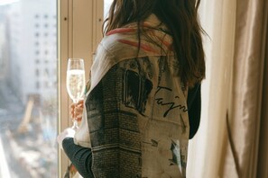 A person holding a glass of champagne near a window with a view of buildings. - Taj Campton Place (San Francisco)