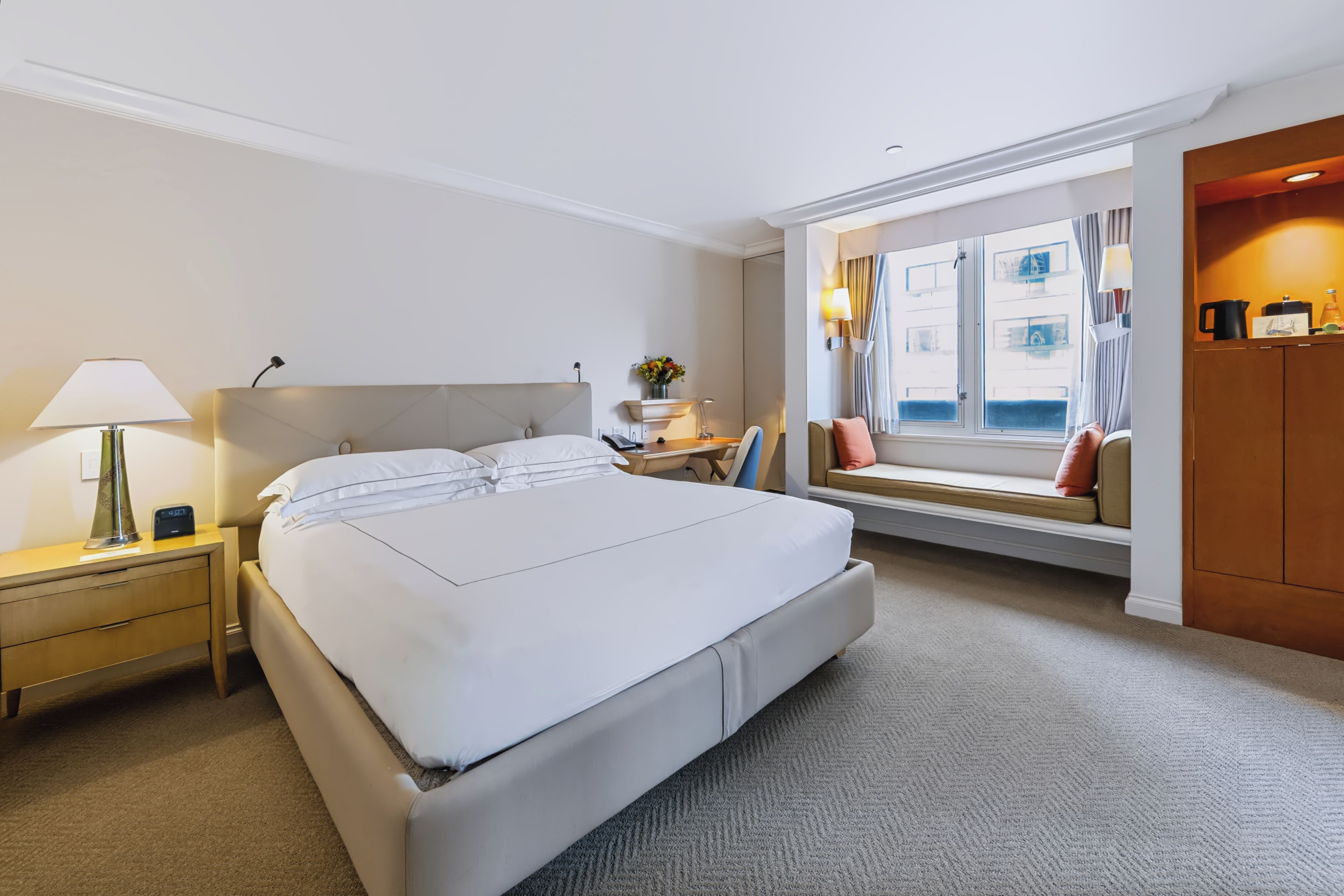 A hotel room with a large bed, bedside tables, a desk, a chair, a window with curtains, and a view of the outside.