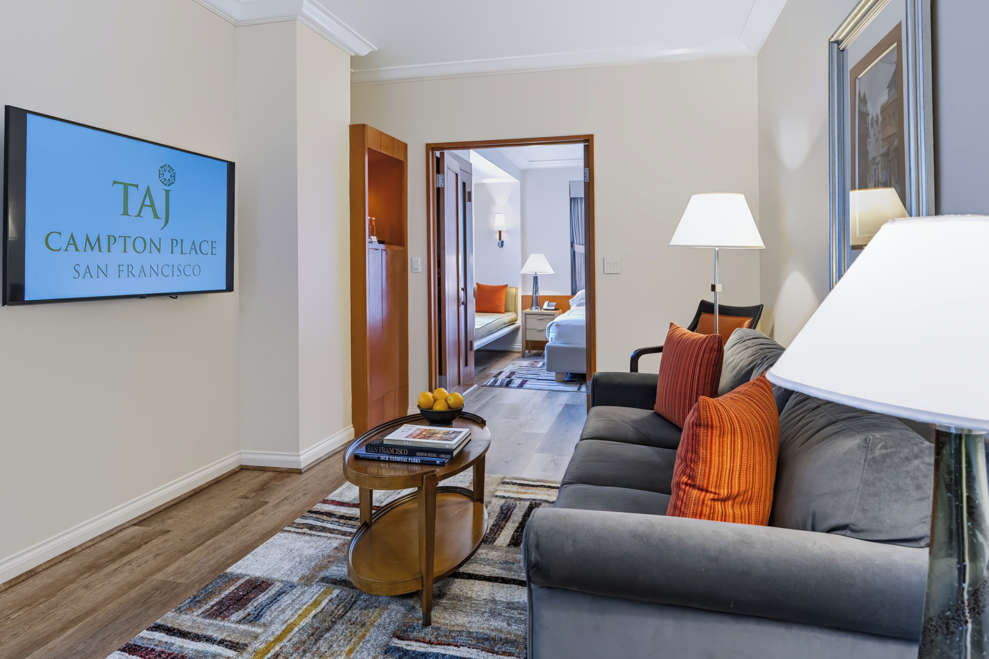 A hotel room with a sofa, a table with books, a lamp, and a bed.