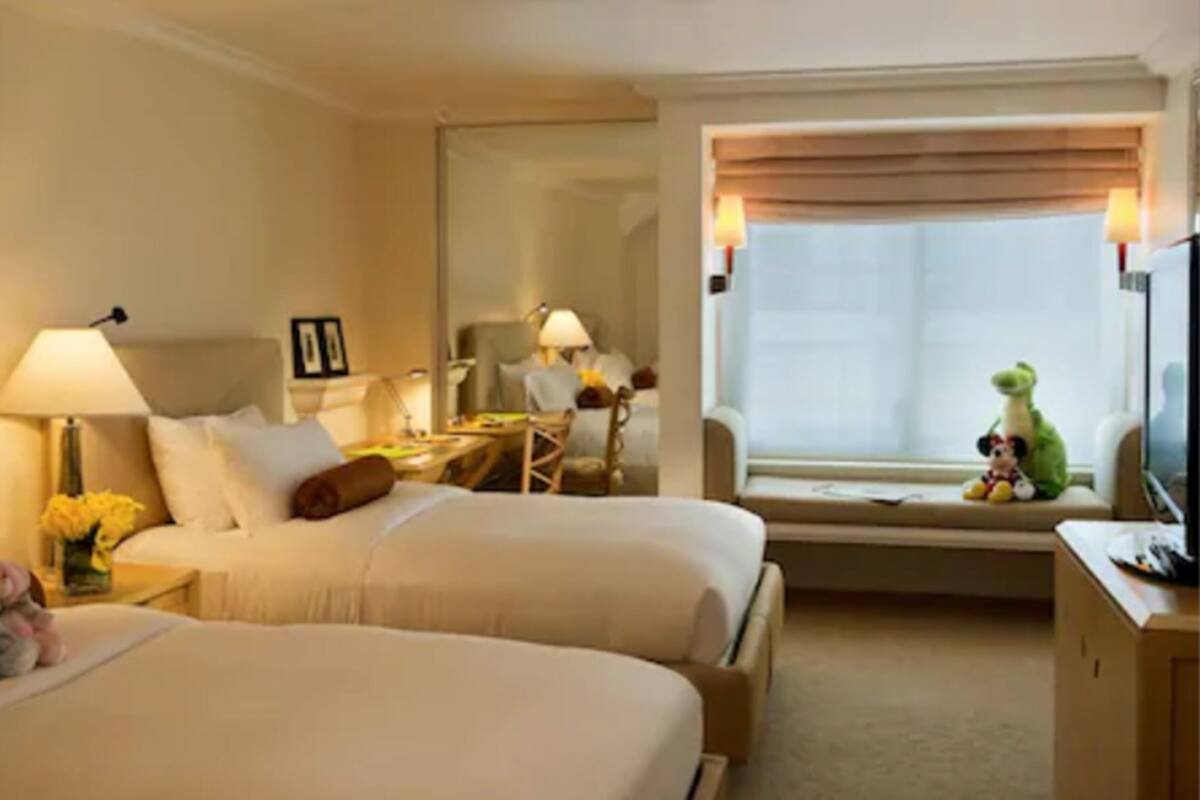A hotel room with two beds, a desk, a chair, a window with a view, and a television.