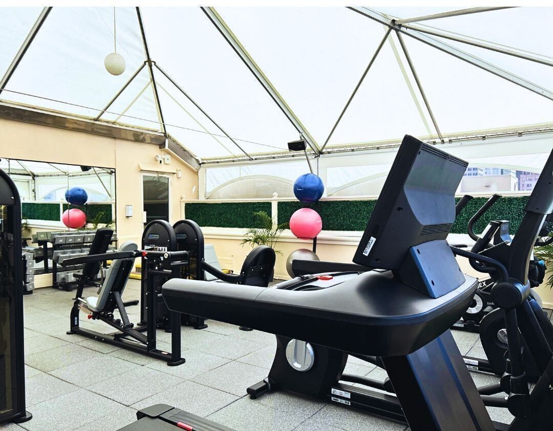 A gym with exercise equipment, including treadmills and weight machines, under a glass roof.
