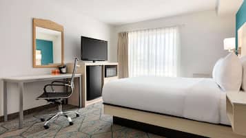 Habitación de hotel con cama, escritorio con silla, televisión y un amplio ventanal con cortinas.